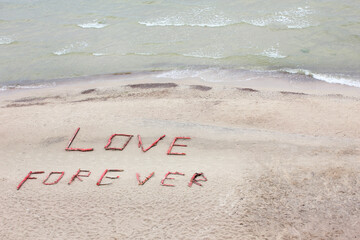 Love forever lettering on the beach with sea and waves. Romantic  background. Concept for love. Copy space. Top view.