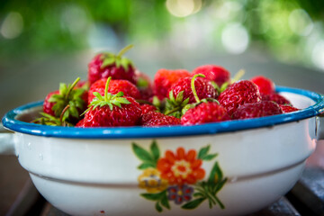 Plate with group of ripe, delicious strawberry on a brown wooden table. Selective focus. Shallow DOF. Blurred natural background