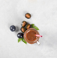 Plum smoothie in a glass jar with bamboo straws on a light gray background top view
