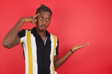 African american man with braids wearing casual shirt over isolated red background confused and...