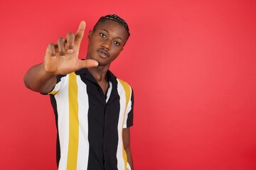 African american man with braids wearing casual shirt over isolated red background making fun of people with fingers on forehead doing loser gesture mocking and insulting.