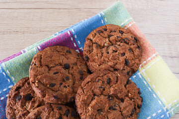 Three chocolate chip cookies on a multi-colored checkered tablecloth. Cookies with chokolate on a table