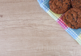 Chocolate chip cookies on a checkered tablecloth and wooden surface with place for text.