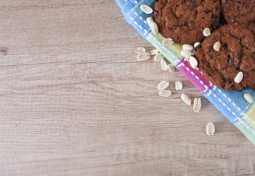 Chocolate chip cookies, peanuts on a checkered tablecloth and wooden surface with slace for text.