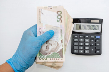 Calculator and a hand in a blue glove holding money banknotes 500 hryvnia on a white background....