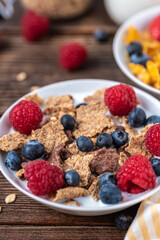 Granola with blueberries and raspberries in white bowl on dark white desk.
