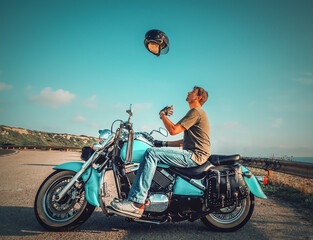 Fototapeta na wymiar Biker sitting on a classic motorcycle tossing the helmet