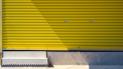 Sunlight and shadow on yellow roller shutter door surface with 2 small steps on cement floor 