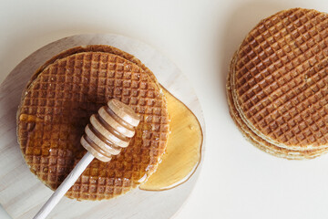 Honey dipper pouring honey over a pile of waffles on a wooden tray