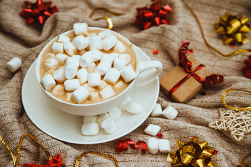 Coffee with marshmallows on a background of knitted fabric with gifts and holiday bows.Hot winter drink.