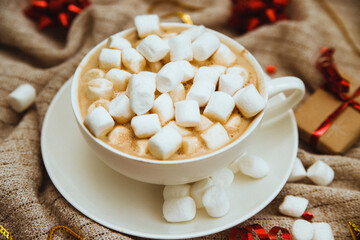 Coffee with marshmallows on a background of knitted fabric with gifts and holiday bows.Hot winter drink.