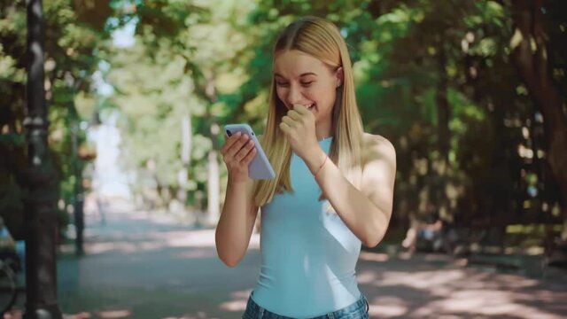 Beautiful young woman stand use phone in the park. Feel happy. Smiling. Internet smartphone. Technology. Outdoor online telephone sunlight close Slow motion.