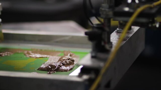 screen printing press with silk screen and brown ink or paint.