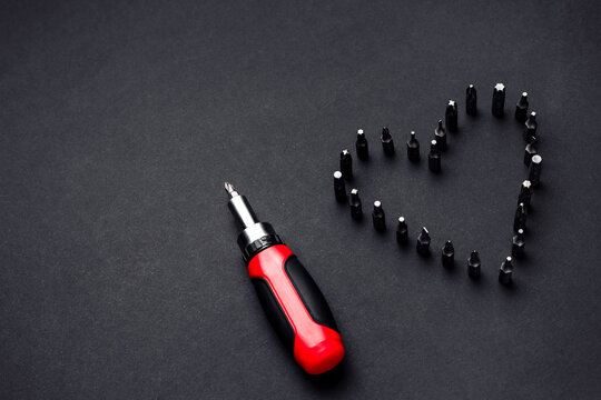 Image of screwdriver an screwdrivers blades arranged in heard shape over black background. Work love concept.
