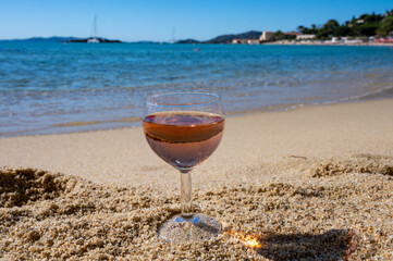 Glass of local rose wine on white sandy beach and blue Mediterranean sea on background, near Le Lavandou, Provence, France
