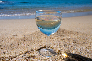 Glass of local dry white wine on white sandy beach and blue Mediterranean sea on background, near Le Lavandou, Provence, France