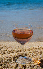 Glass of local rose wine on white sandy beach and blue Mediterranean sea on background, near Le Lavandou, Provence, France