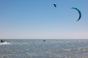 People practicing Kitesurfing. Colorful kites on the sea shore. Blue sea and windsurfing.