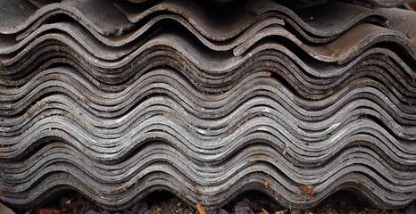 Stack of old asbestos dirty corrugated slate sheets, side view, closeup. Building material removed from roof house during renovation