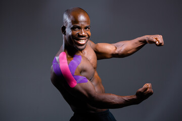 Obraz premium African American with kinesio tape on his shoulder shows biceps and smiles