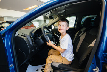 In a car dealership, a happy boy is driving a new car. Car purchase