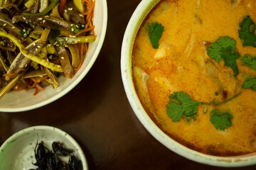 Tom yum, pork ears salad and a plate of crickets on a wooden table
