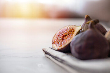 Fresh purple fig fruit and slices with sun background. Whole figs and one fig sliced in half on top of a teak garden table. Focus is on the sliced fig.