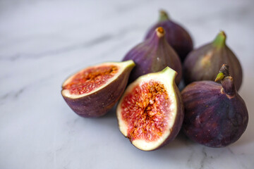 Whole figs and one fig sliced in half on top of a teak garden table. Focus is on the sliced fig. Ripe sweet figs with green leaves. Healthy mediterranean fig fruit.