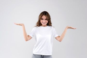 Smiling young woman standing against white background and holding her hands up as scales for...