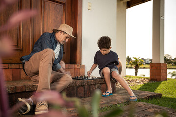Garoto joga de xadrez com seu avô na escada de casa.