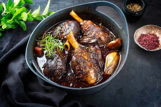 Modern style traditional braised slow cooked lamb shank in red wine sauce with shallots and carrots offered as top view in a design stewpot