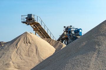 Naklejka na ściany i meble Conveyor belt over heaps of gravel against the blue sky at an industrial cement plant.