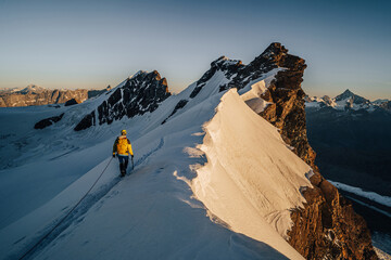 An alpinist climbing a rocky and snow mountain ridge during sunrise. Mountaineering and alpinism in...