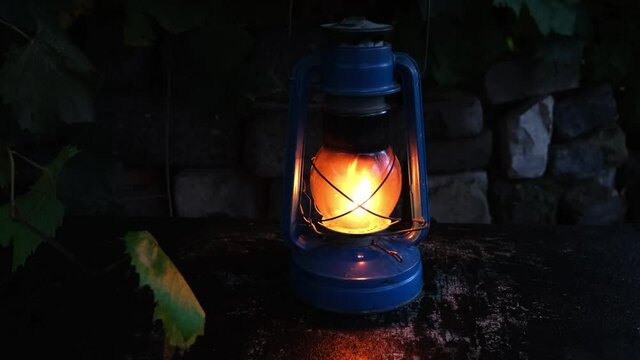 Burning kerosene lamp against a stone wall and a vine branch swaying in the wind.