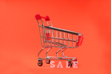 Mini shopping cart with word SALE on a red background. The concept of shopping in stores and online