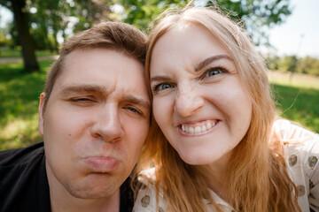 Two lovers making funny selfie, Portrait of cheerful laughing funny young people. Cute couple of hipsters is walking in park. Emotion facial expression. Beautiful sunny day.