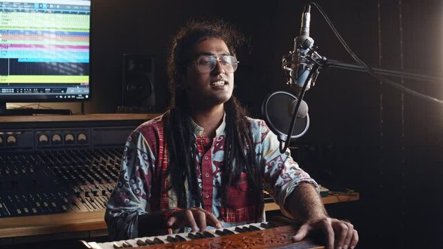 Indian people. Creative world. Hindi man playing harmonium in the sound studio. A long hair brunette male person in a traditional shirt plays meditation music.