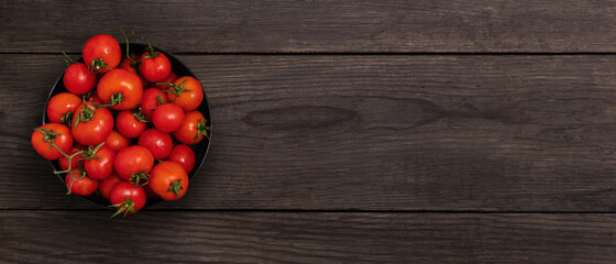 Cherry tomatoes in a black bowl on a dark wooden table, banner.