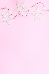 Christmas composition border with white stars on a red white cord, pink background, vertical, copy space, top view