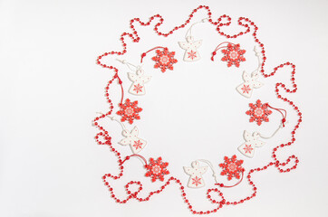 Obraz na płótnie Canvas Christmas wooden toys in the form of a white angel and a red snowflake with red beads are laid out in a circle with a place for copy space with a flat layout on a white background. View from above