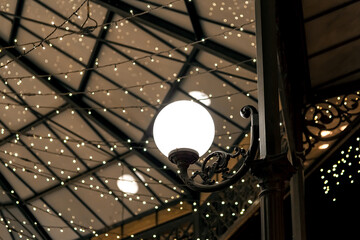 white round lantern on a wrought iron pillar of the restaurant terrace gazebo with garlands on the ceiling, architectural lighting of the room in a retro style, nobody.