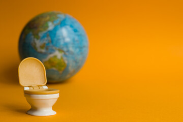 White toilet bowl with orange lid on an orange background with a globe in honor of world toilet day...