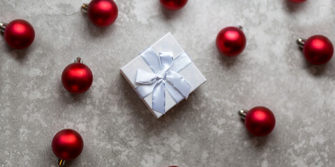 White gift box with white ribbon bow and vinous christmas balls around, isolated on gray background