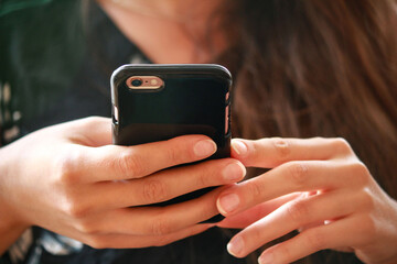 Młoda kobieta trzymająca w dłoniach smartfon w czarnym etui