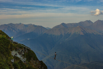 a man in the mountains walks on a stretched bridge. dressed in gear