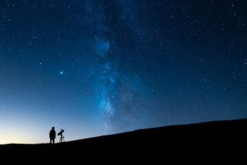 Person observing the blue starry sky with a telescope at night. Silhouette of an astronomer...