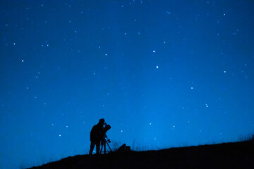Silhouette of a astronomer observing the immensity of the universe and the stars. Astronomy lover with a telescope observing the blue starry sky at night.