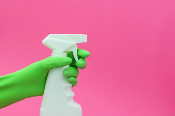 Kitchen cleaner in hand, hand with a green glove. On a pink background.