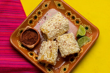 Mexican corn on the cob also called elotes with cheese and mayonnaise on yellow background