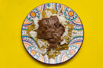Mexican green chilaquiles with cecina beef steak on yellow background